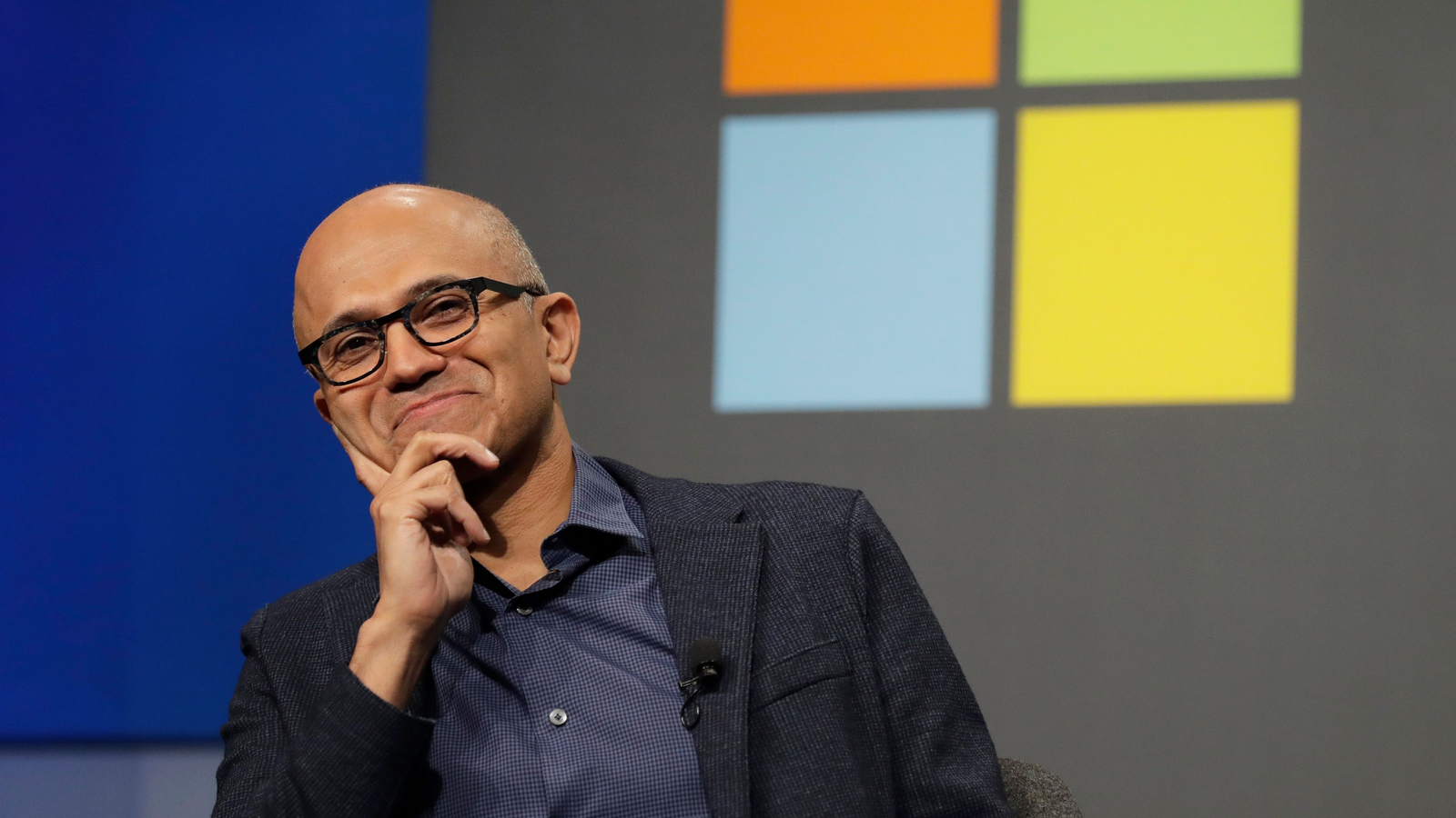 Satya Nadella sitting with Microsoft logo at the background
