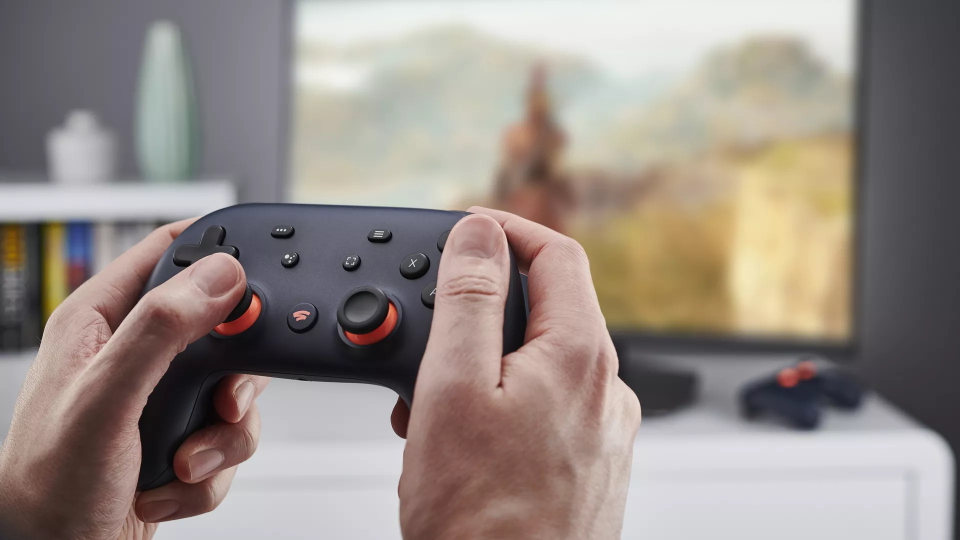 A person holding Stadia controller with a TV in background